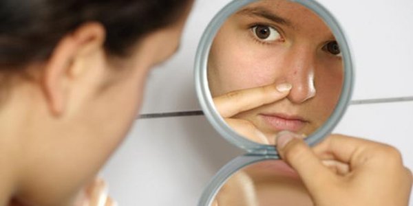 Frau sieht einen Eiterpickel in der Nase im Spiegel