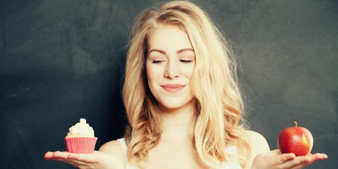 Frau hält in der einen Hand ein Cupcake und in der anderen ein Apfel 