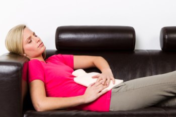 Schmerzen am Bauchnabel Therapie Auf dem Sofa liegende Frau hält sich eine Wärmflasche auf den Bauch
