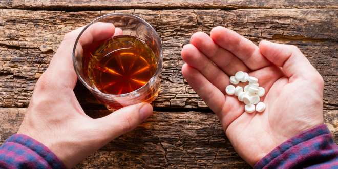 Person hält Tabletten und Glas mit Whisky