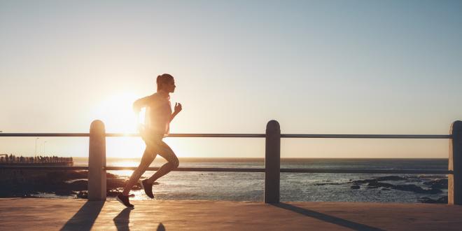 Frau joggt bei Sonnenuntergang am Strand entlang und verbessert so ihre Ausdauerleistung