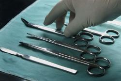 Das Bild zeigt ein OP-Tischchen mit sterilisiertem OP-Besteck und eine Hand in sterilen Handschuhen, welche nach eines der Instrumente greift