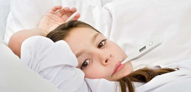 Kind liegt mit Fieberthermometer im Mund im Bett