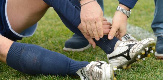 Fußballspieler sitzt auf dem Rasen und hält sich den Knöchel