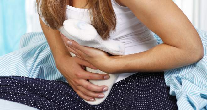 Bauchschmerzen im Sitzen Sitzende Frau hält sich Wärmflasche auf den Bauch