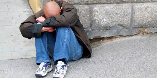 Drogen können vielfältige Folgen aufweisen. Trauernder Mann sitzt auf dem Gehweg